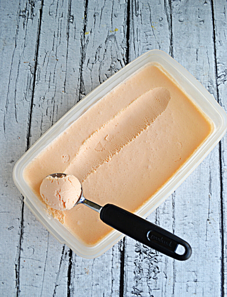 A container of Thai Tea Ice Cream with an ice cream scooper in it scooping out the ice cream. 