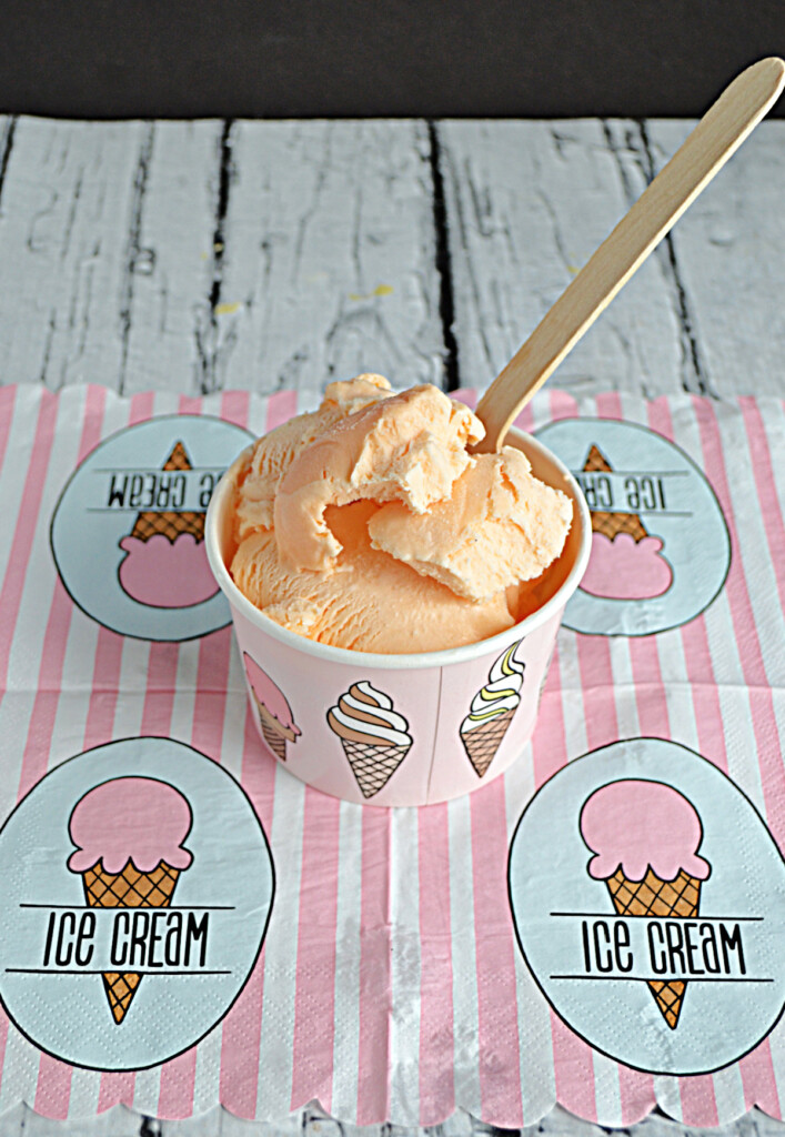 A pink and white ice cream napkin with a bowl of Thai Tea Ice Cream with a wooden spoon in it. 