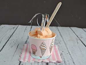A cup of Thai Tea Ice Cream with a wooden spoon and silver streamer on top.