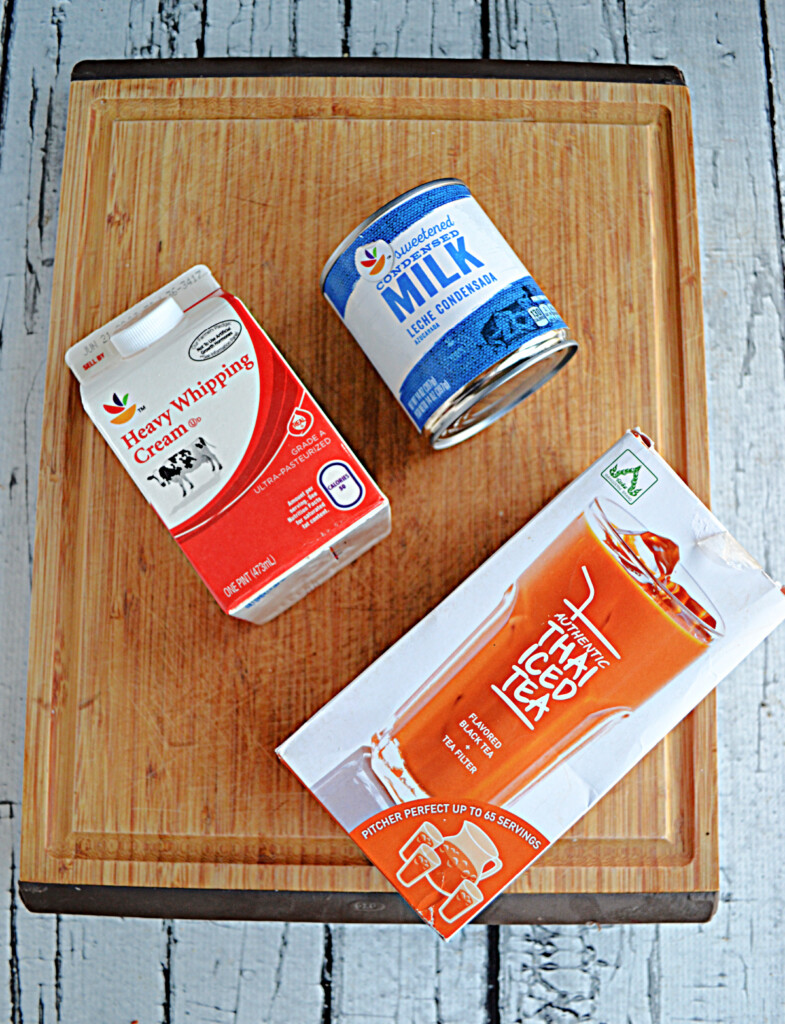 A cutting board with a carton of heavy cream, a can of ssweetened condensed milk, and Thai Tea Mix.