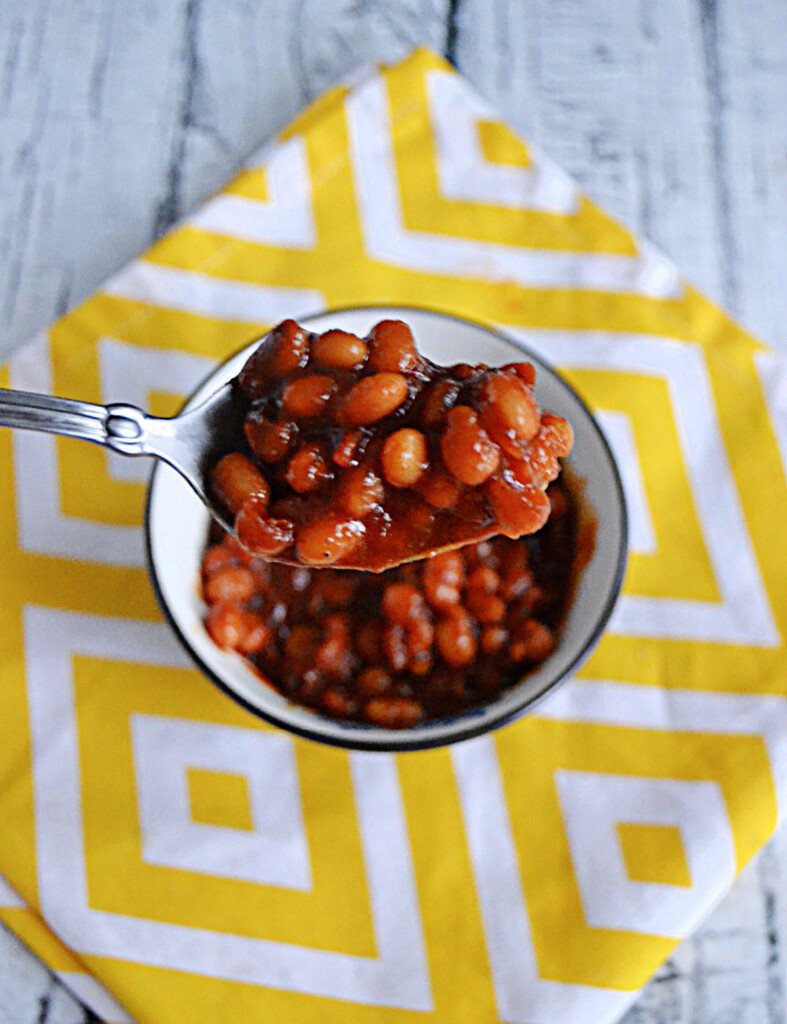 A close up of a spoonful of baked beans with the bowl in the background.