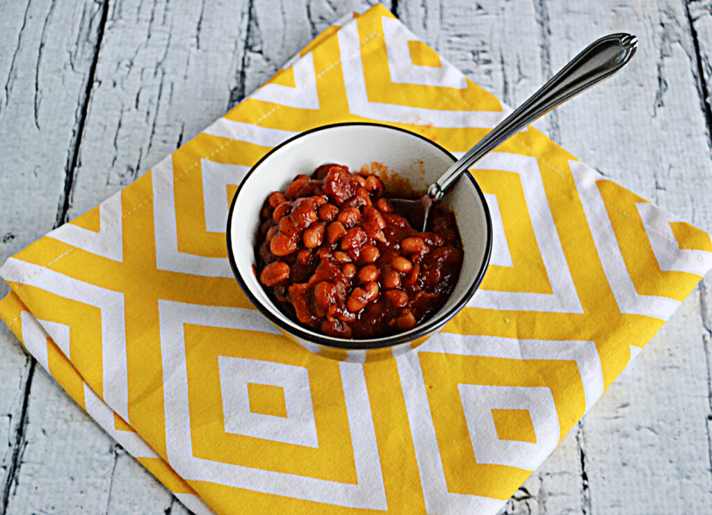 A bowl of baked beans with a spoon in it.
