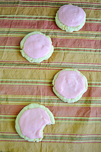 Four cookies with pink icing with one having a bite out of it.