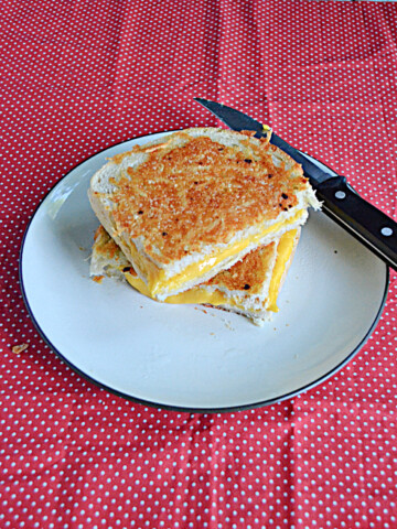 A grilled cheese sandwich cut in half, on a plate, with a knife behind it.