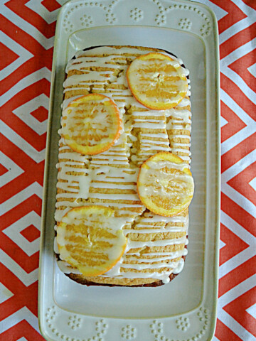 A white platter with an Orange Pound Cake loaf drizzled with glaze and orange slices.