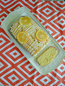 A white platter with an Orange Pound Cake Loaf on top drizzled with glaze and topped with orange slices with a slice of the cake on the platter.