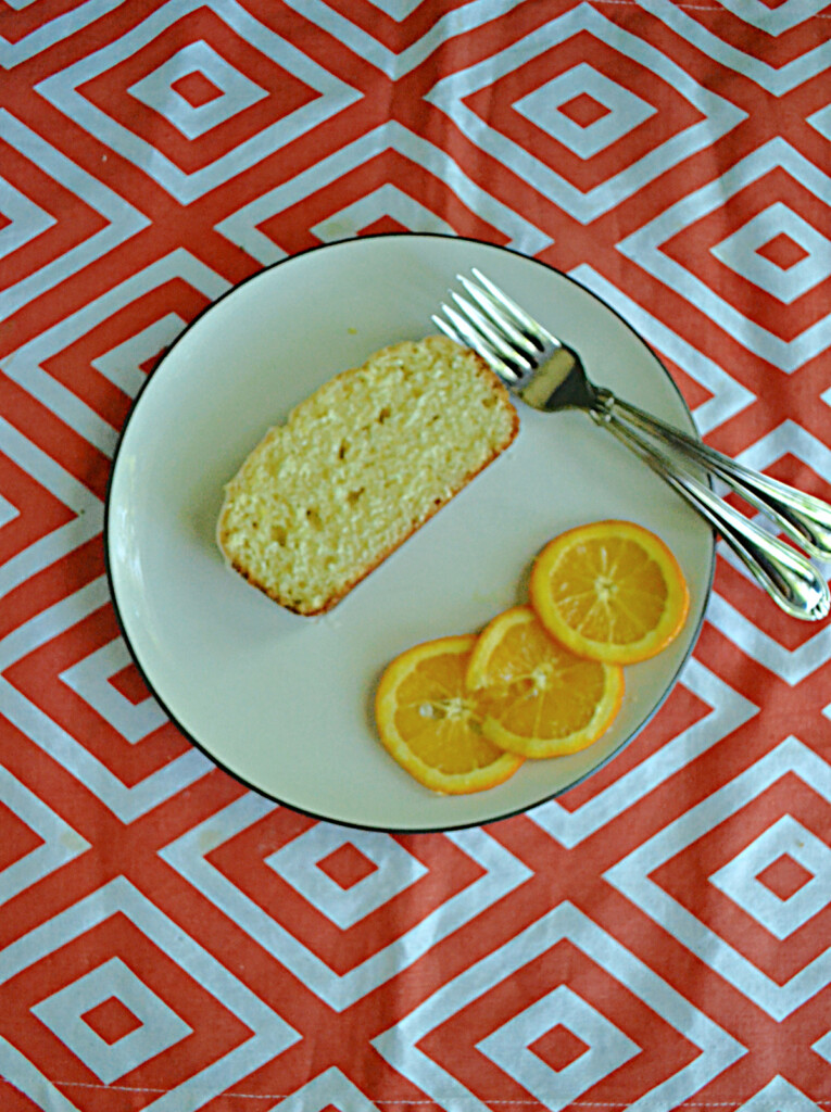 A plate with a slice of orange cake, two forks, and three orange slices. 