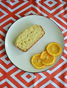 A plate with a slice of orange pound cake and three orange slices on it.