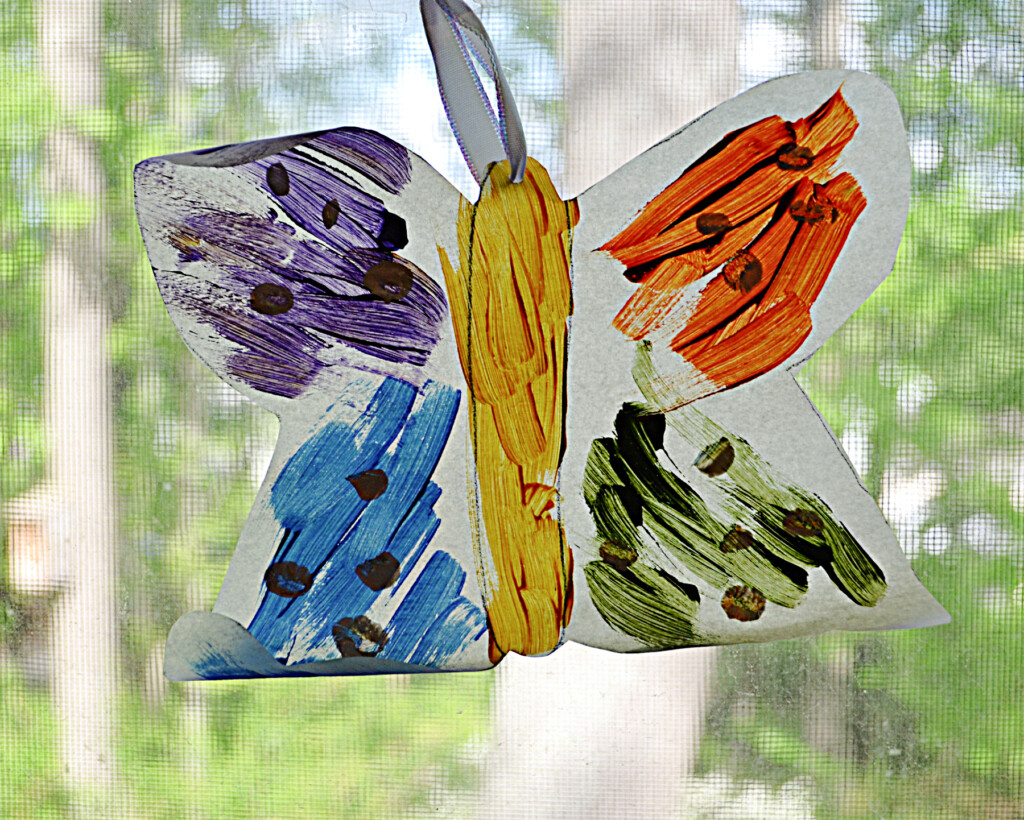 A DIY butterfly suncatcher painted and hanging in a window.