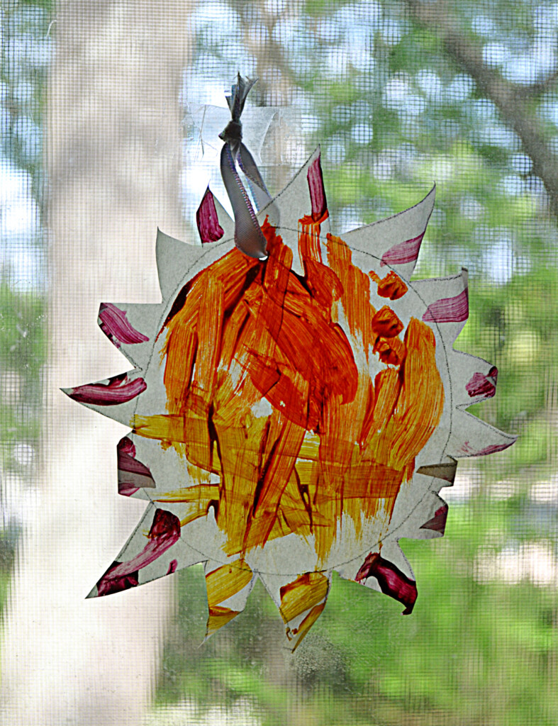 A DIY sun suncatcher painted and hanging in a window.