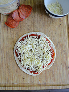 A tortilla topped with pizza sauce annd mozzarella cheese.