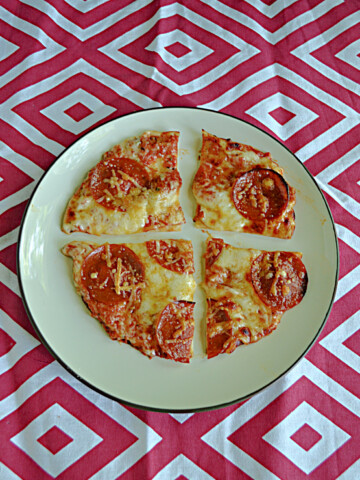 A plate with a pepperoni tortilla pizza cut into quarters.