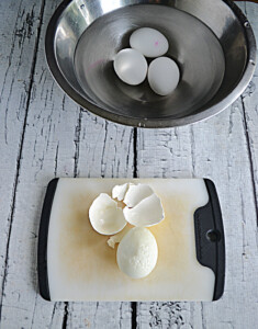A bowl of hard boiled eggs and one egg with the shell taken off.