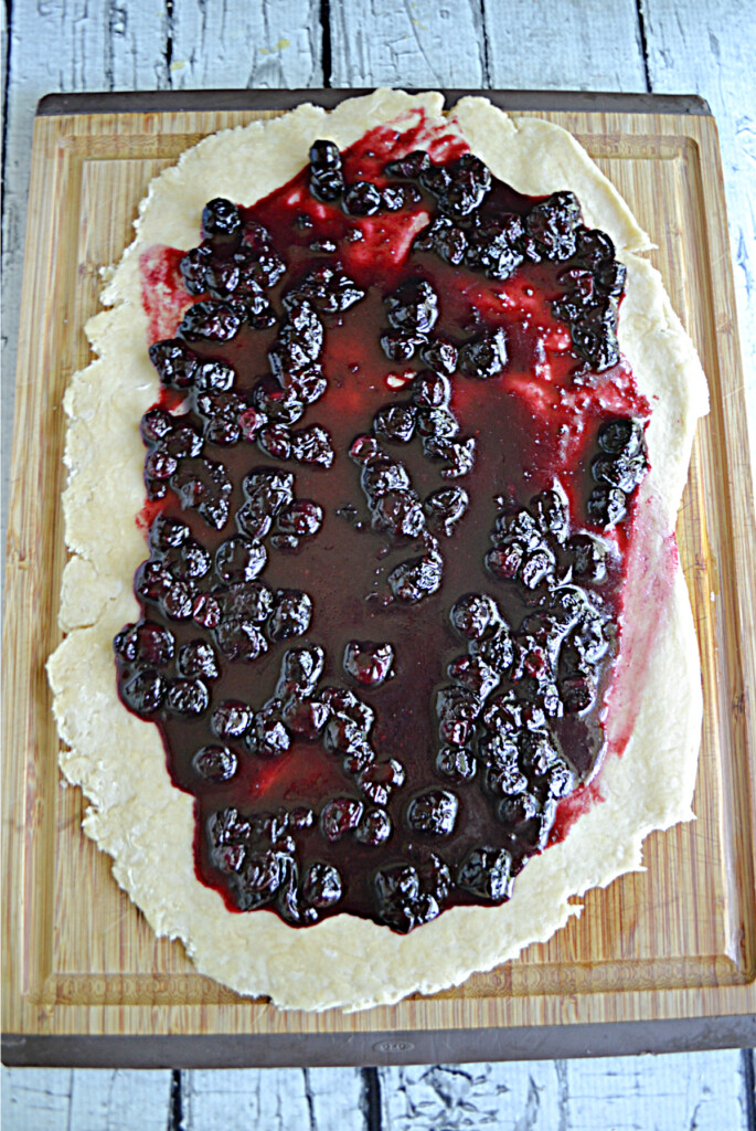 Bread dough rolled out with blueberry jam on it.