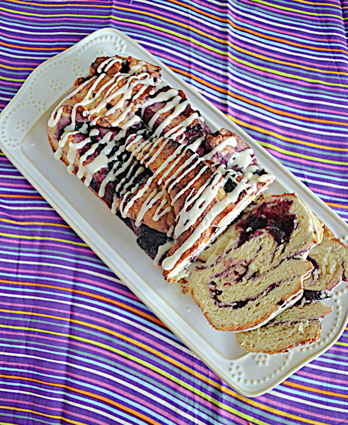 A top view of a platter with a Blueberry Babka on it with two slices cut and laying down on the platter.