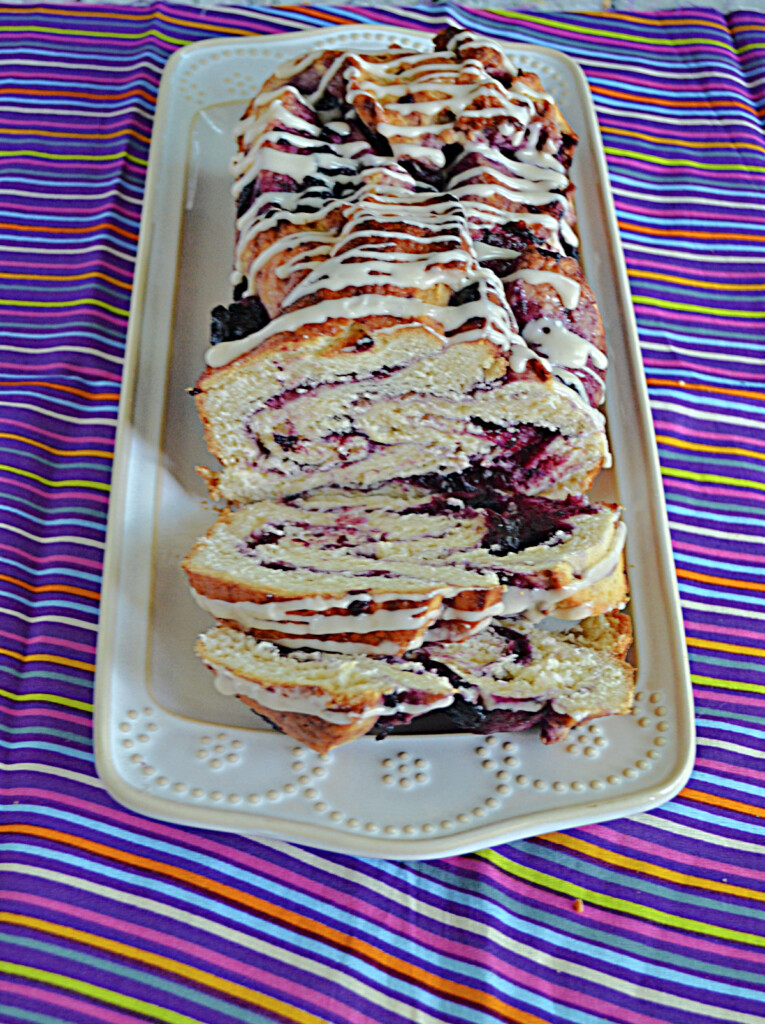 A close up front view of a platter with a Blueberry Babka on it with two slices cut and laying down on the platter.