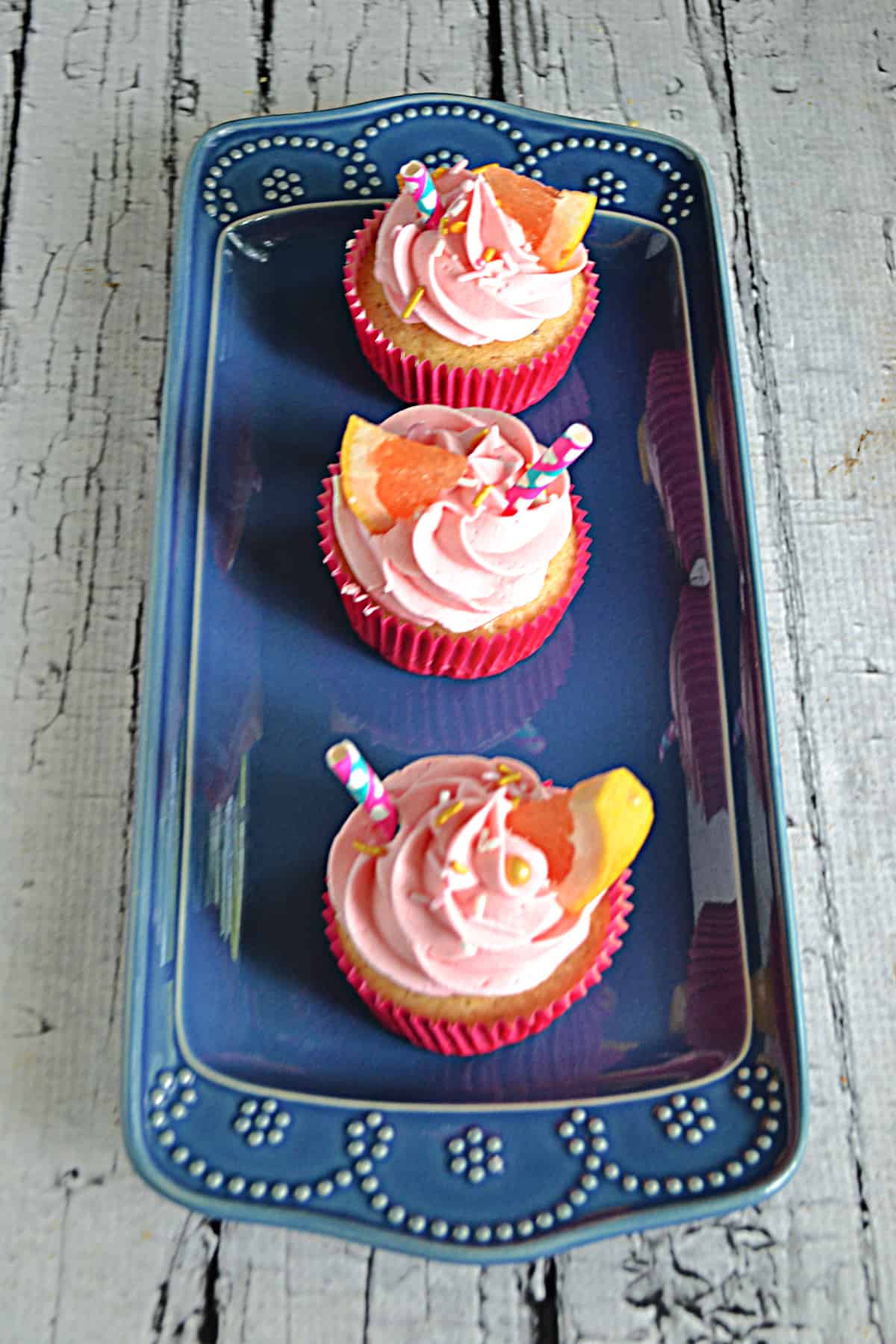 A blue platter with three pink grapefruit cupcakes on it.