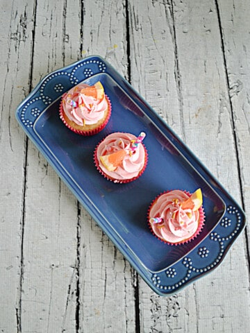 A blue platter with three pink grapefruit cupcakes with straws in them.