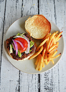 A plate with a veggie burger topped with lettuce, tomatoes, and onions and fries on the side.