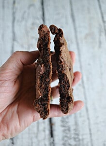 A hand holding a brownie batter cookie broken in half.
