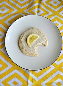 A plate with a lemon cookie with a bite out of it.