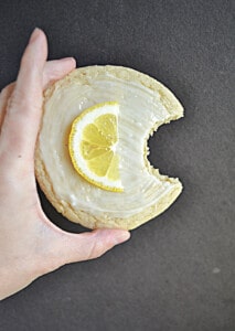 A hand holding a lemon cookie with a bite taken out of it.