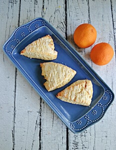 A platter with three orange scones and oranges behind it.