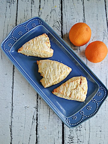 A platter with three orange scones and oranges behind it.