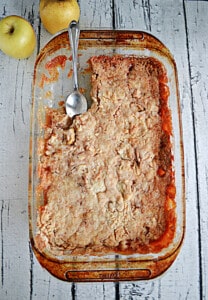 A glass baking dish with apple cake and a spoon in the dish.