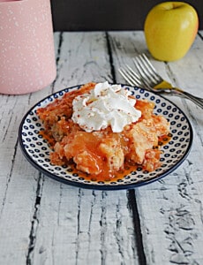 A plate with a pile of Apple DUmp Cake covered in caramel sauce and whipped cream on top.
