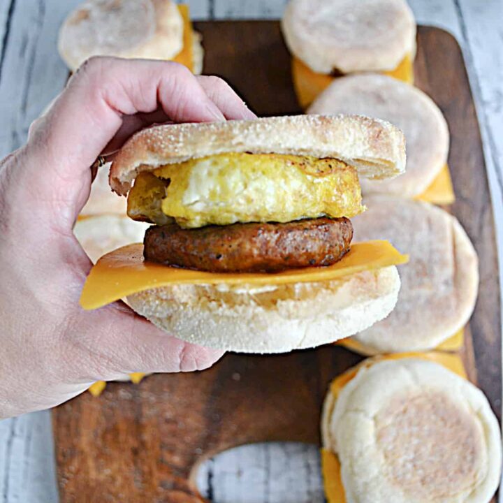 A close up of a hand holding an egg, sausage, and cheese breakfast sandwich.