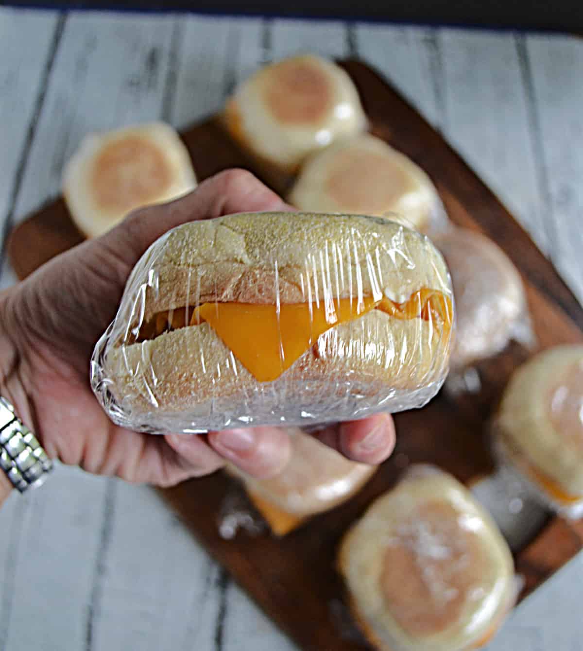 A close up of a hand holding a plastic wrapped sausage and cheese breakfast sandwich.