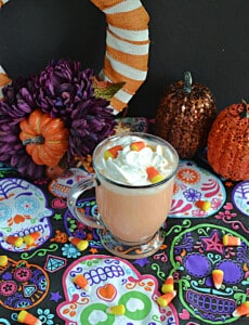 A mug of orange candy corn hot chocolate topped with whipped cream and candy corn.