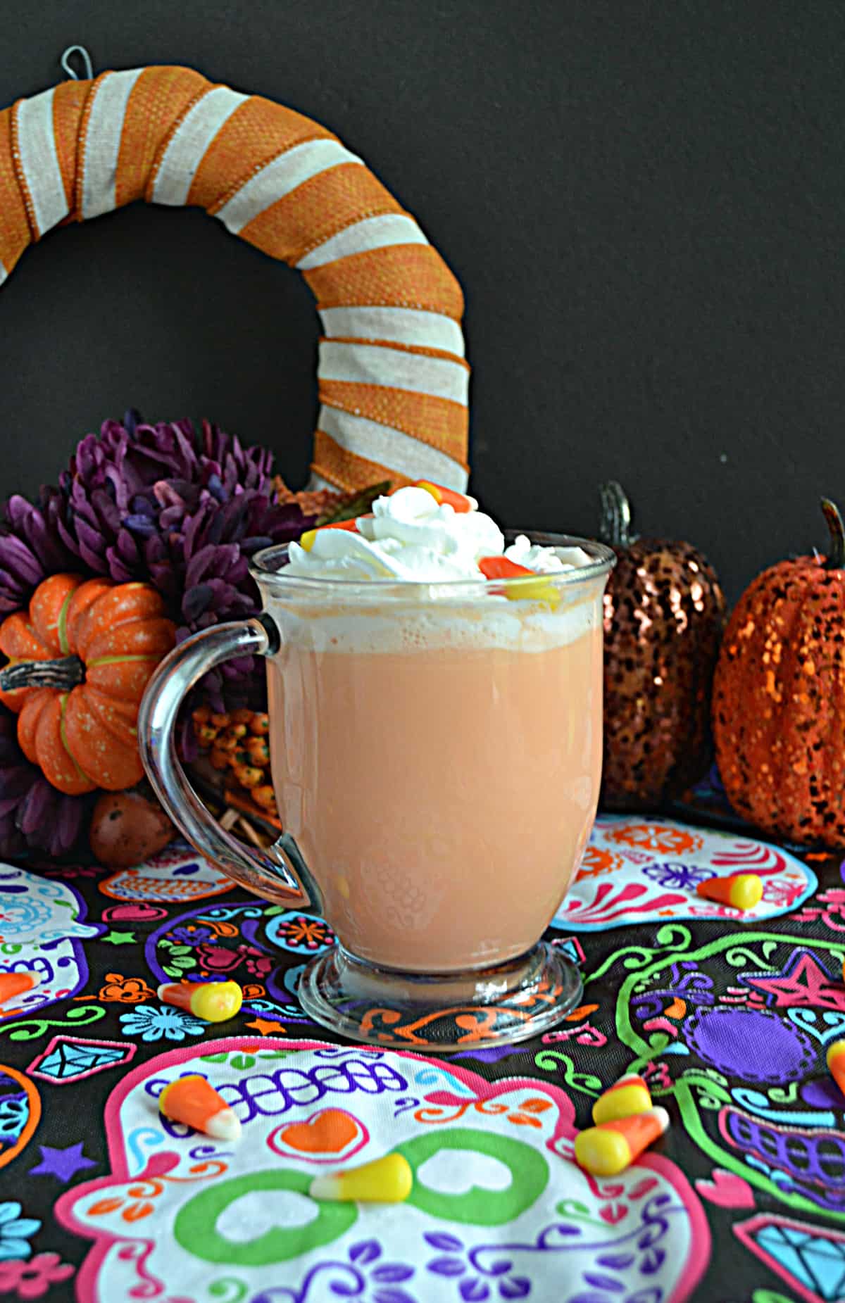 A close up view of a mug of orange candy corn hot chocolate topped with whipped cream and candy corn.