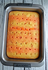 A cake with holes poked in it and yellow and orange Jell-O stripes on it.