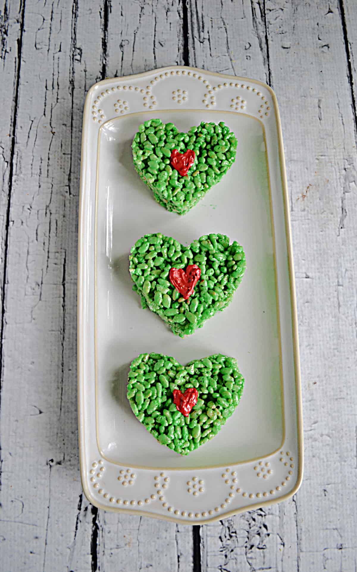 Three green heart shaped Rice Krispies Treats with a red heart in the middle.