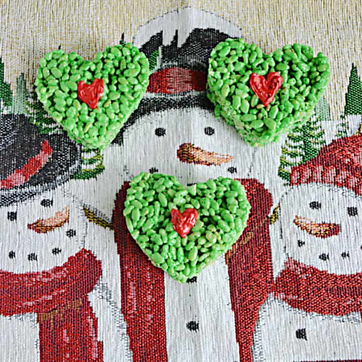 Three green heart shaped Rice Krispies Treats with a red heart in the middle on a snowman background.