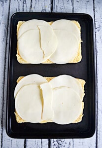 A sheet pan with 6 rolls topped with provolone cheese.