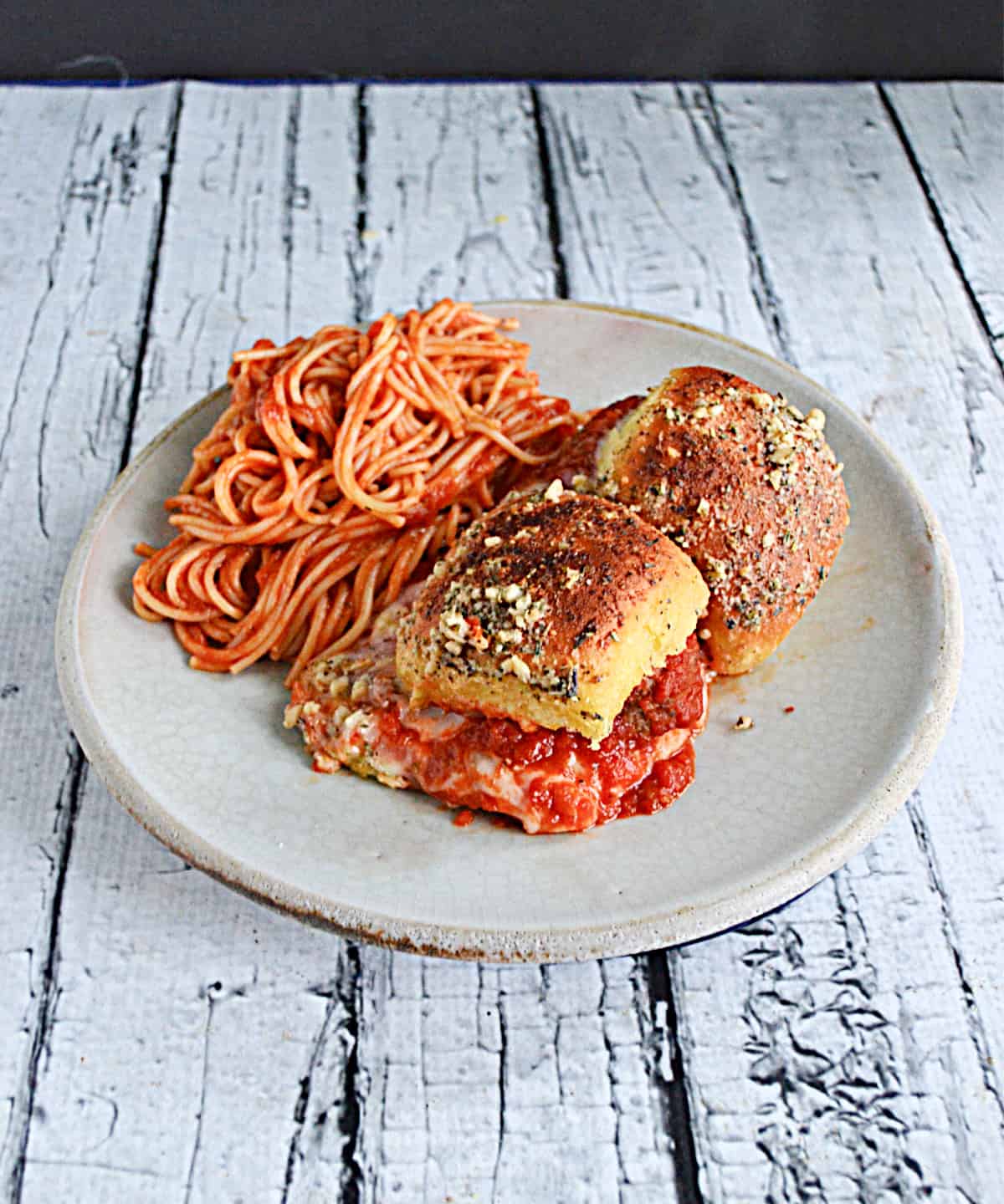A plate with two meatball sliders and a side dish of spaghetti.