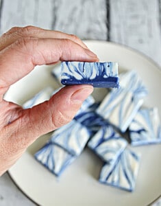 A hand holding a piece of bue and white fudge with a bite taken out of it.