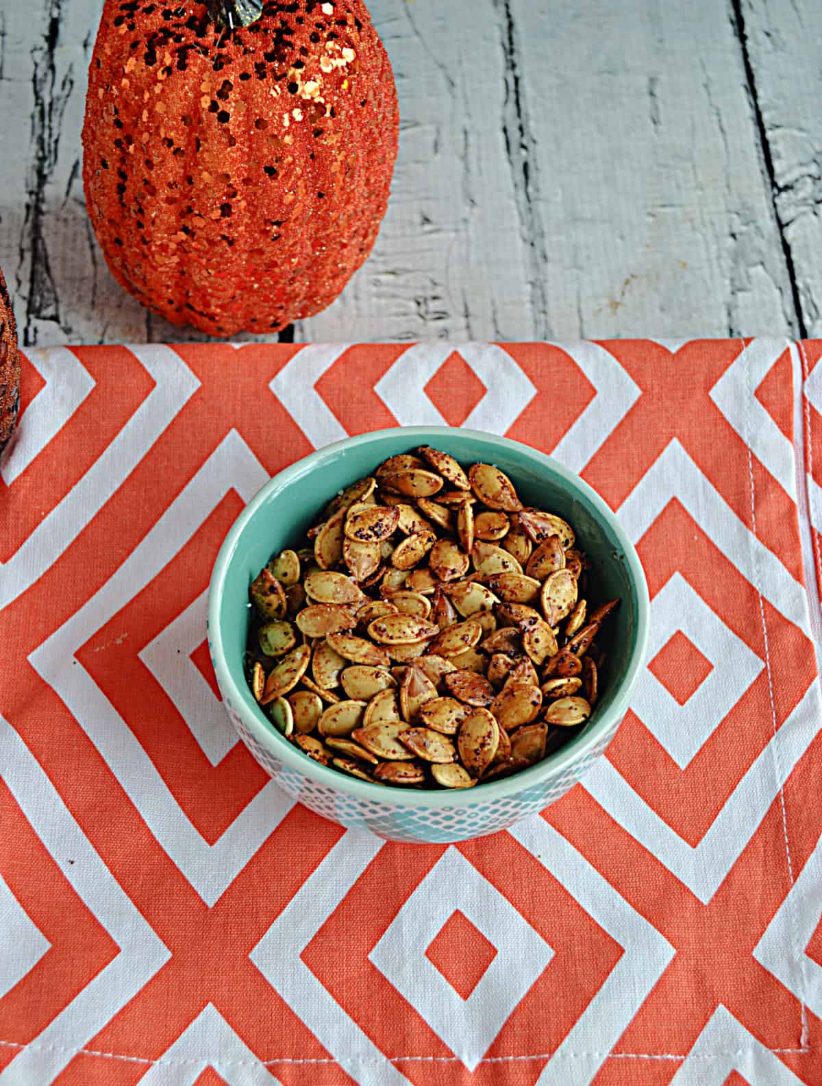 A bowl of roasted pumpkin seeds with a sparkling pumpkin behind it.