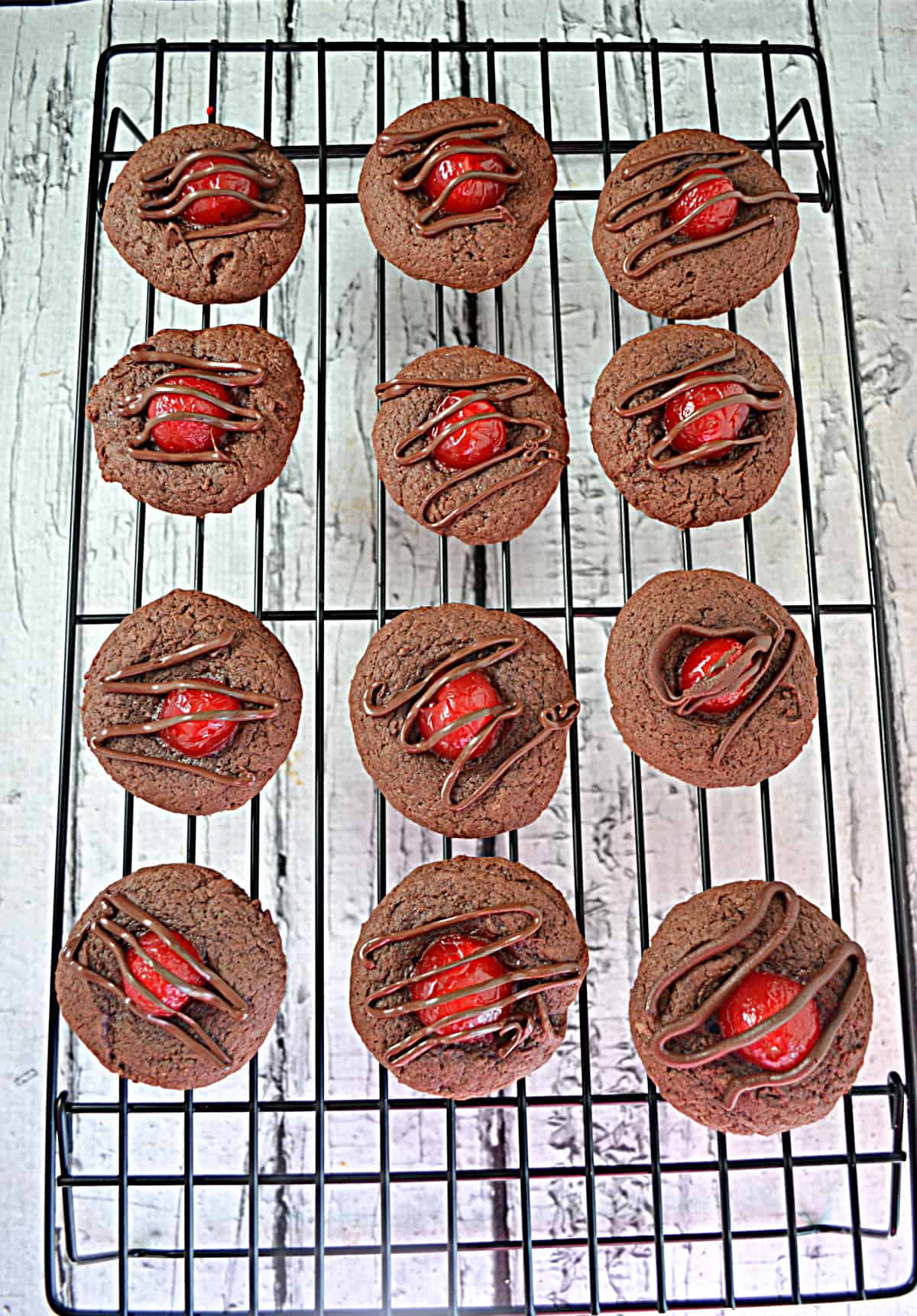 A baking rack holding 12 chocolate covered cherry thumbprint cookies