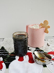 A jar of gingerbread syrup next to a coffee cup with a gingerbread latte in it.