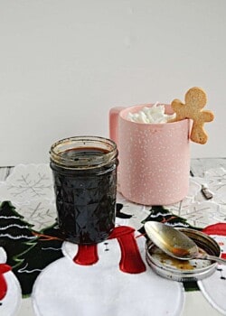A jar of gingerbread syrup next to a coffee cup with a gingerbread latte in it.