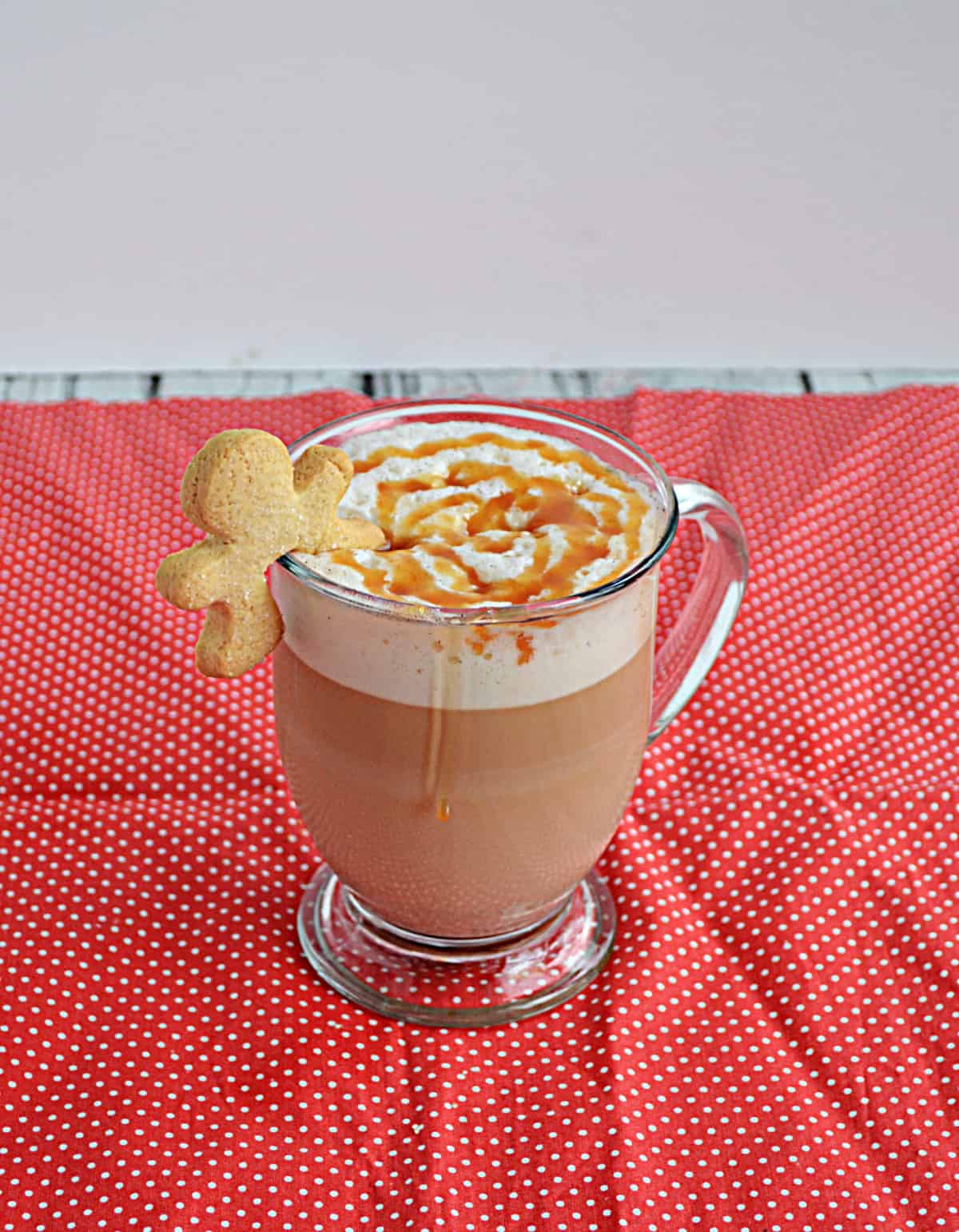 A mug of Gingerbread Latte with a caramel drizzle and a gingerbread man on the rim.