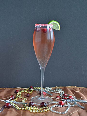 A glass of Cranberry Champagne Cocktail with beads around the base of the glass.