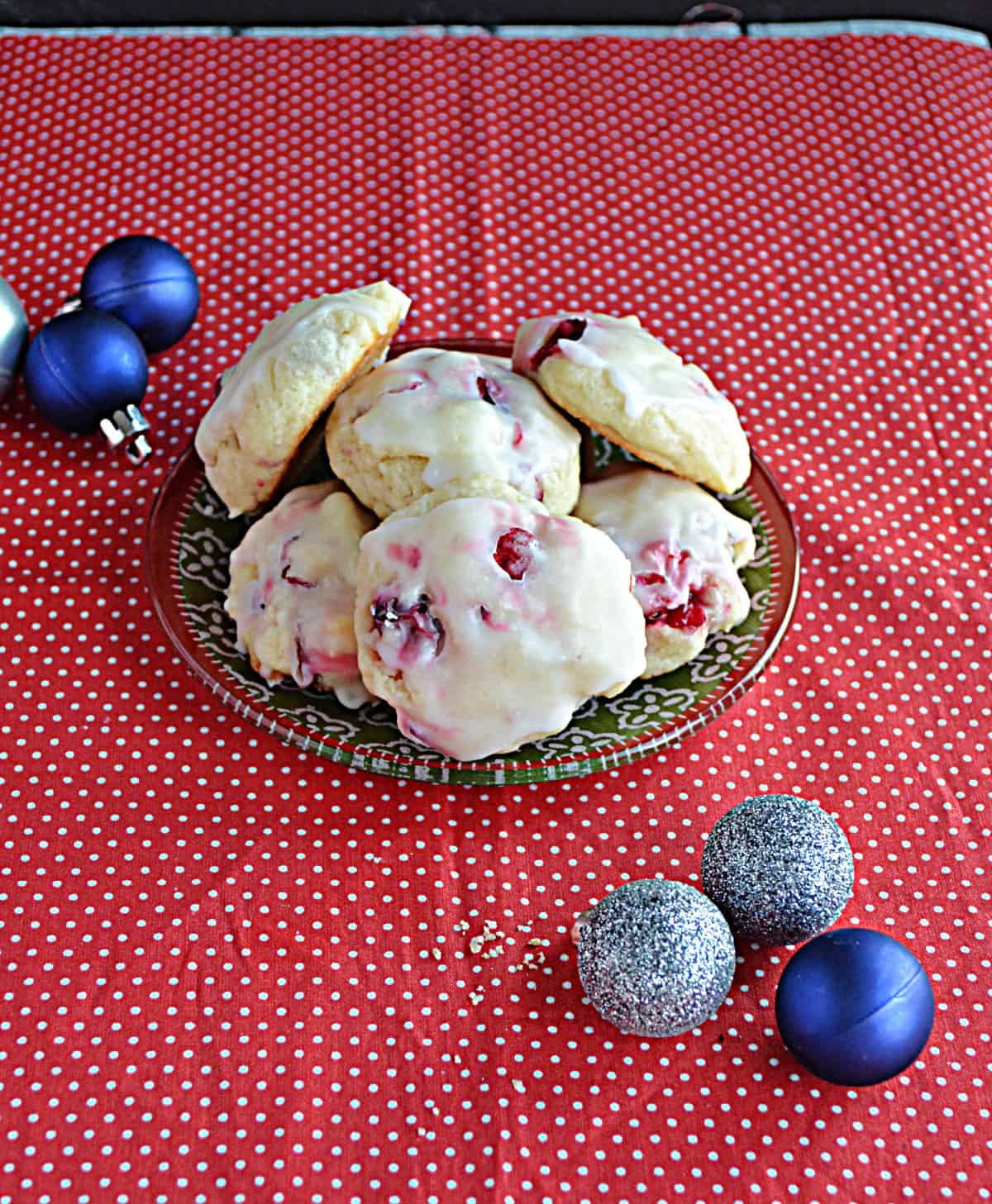 A plate piled high with lemon cranberry cookies and Christmas ornaments around the plate.