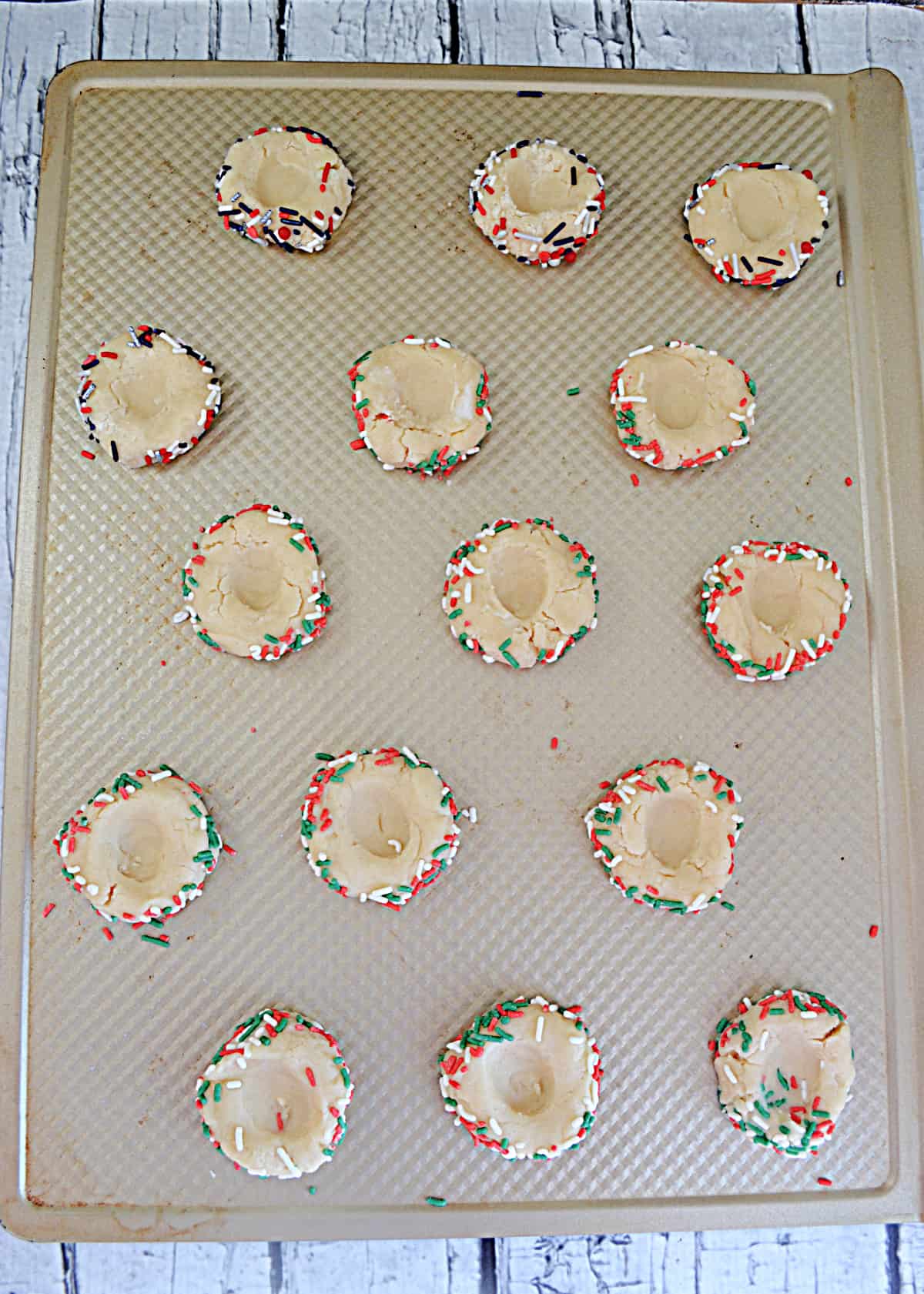 A cookie sheet with unbaked thumbprint cookies on it. 