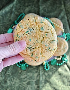 A close up of a hand holding a St. Patrick's Day cookie with green sprinkles.