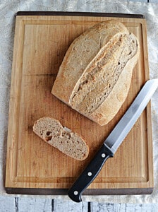 A loaf of sourdough bread with a slice cut off next to a knife.